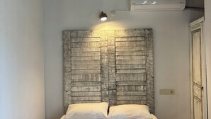 A single bed with a wooden headboard, a wall-mounted air conditioner, and a bedside lamp. - Assos Gül pansiyon (Ayvacik)