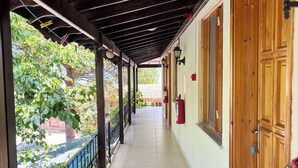 A covered corridor with a tiled floor, wooden doors, and a blue railing. - Assos Gül pansiyon (Ayvacik)