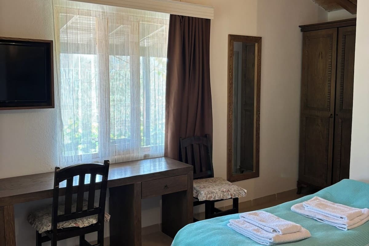 Um quarto com cama, escrivaninha, cadeira, televisão e guarda-roupa.