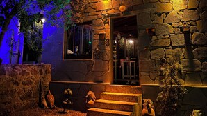 A stone building with a staircase leading to the entrance, surrounded by greenery and potted plants. - Assos Gül pansiyon (Ayvacik)