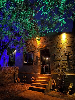 A stone building with a staircase leading to the entrance, surrounded by greenery and potted plants. - Assos Gül pansiyon (Ayvacik)