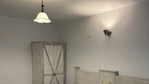A hotel room with two beds, a wardrobe, a nightstand, a wall-mounted light, and a ceiling light fixture. - Assos Gül pansiyon (Ayvacik)