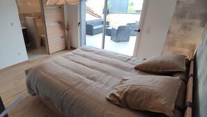 Un dormitorio moderno con una cama grande, una puerta corredera que da a un balcón y vistas a un área de estar exterior.