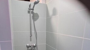 Un petit espace douche fermé, avec des carreaux gris et un sol blanc.