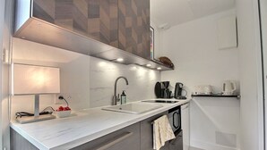 A modern kitchen with a white countertop, a sink, a coffee maker, and a towel hanging on the door.