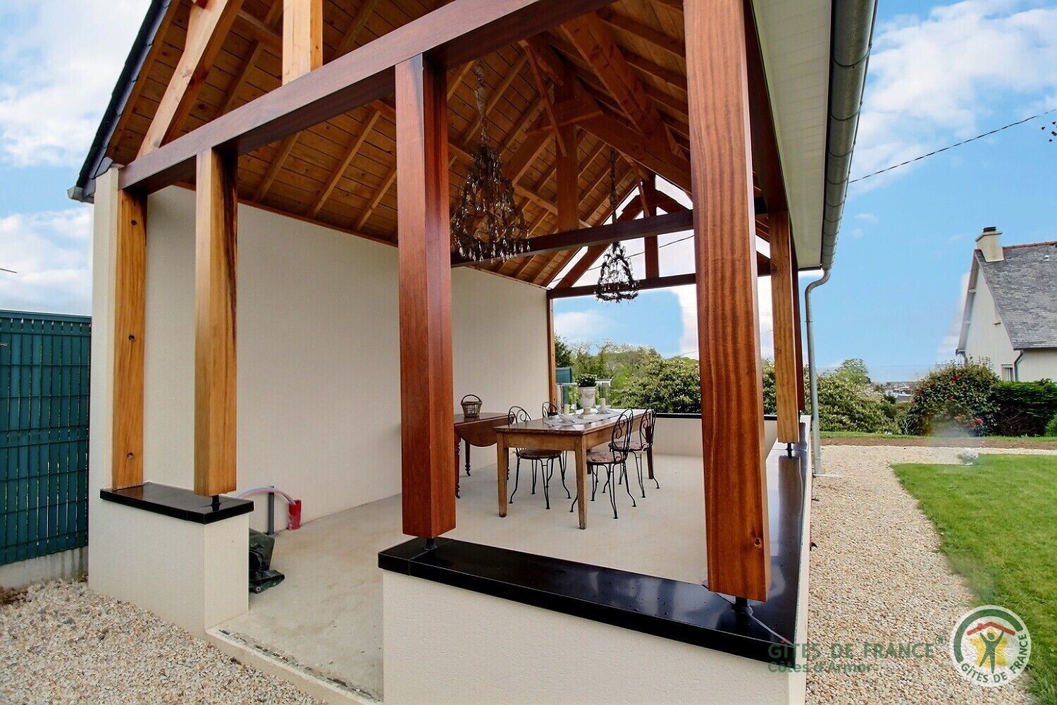 Un área de comedor al aire libre cubierta, con una mesa y sillas, vigas de madera y vistas del paisaje circundante.