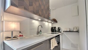 Una cocina moderna con encimera blanca, un fregadero, una cafetera y una toalla colgada en la puerta.