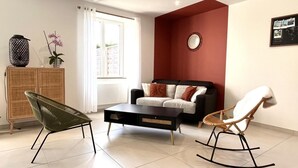 Una sala de estar moderna con un sofá, dos mecedoras, una mesa de centro, un aparador y una ventana con cortinas.