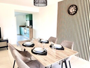 Un coin repas avec une table en bois dressée pour quatre personnes, une cuisine en arrière-plan et un mur à rayures.