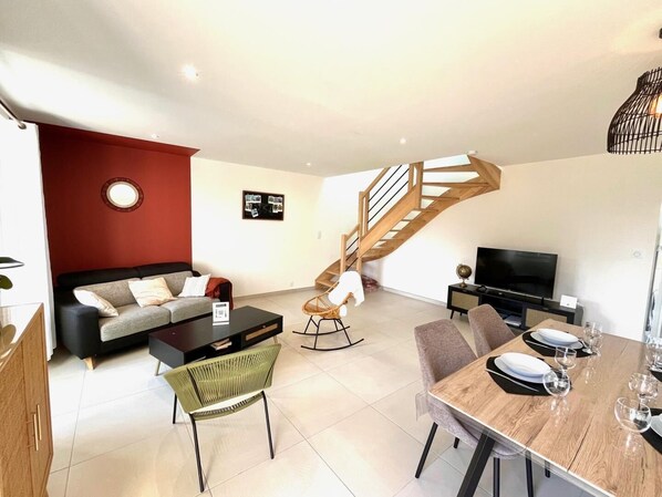 Un salon moderne comprenant un canapé, une table basse, un ensemble de table à manger, un téléviseur et un escalier.