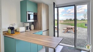 Cocina compacta con microondas, tostadora y cafetera, y una puerta corrediza de vidrio que da a un patio exterior con mesa de picnic.