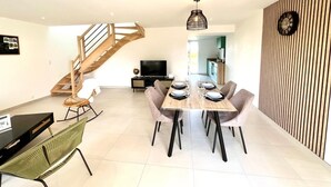 Una sala de estar moderna con comedor, una escalera, un televisor de pantalla plana y una cocina al fondo.
