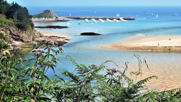 Un paisaje costero con una playa arenosa, afloramientos rocosos y un mar azul cristalino.