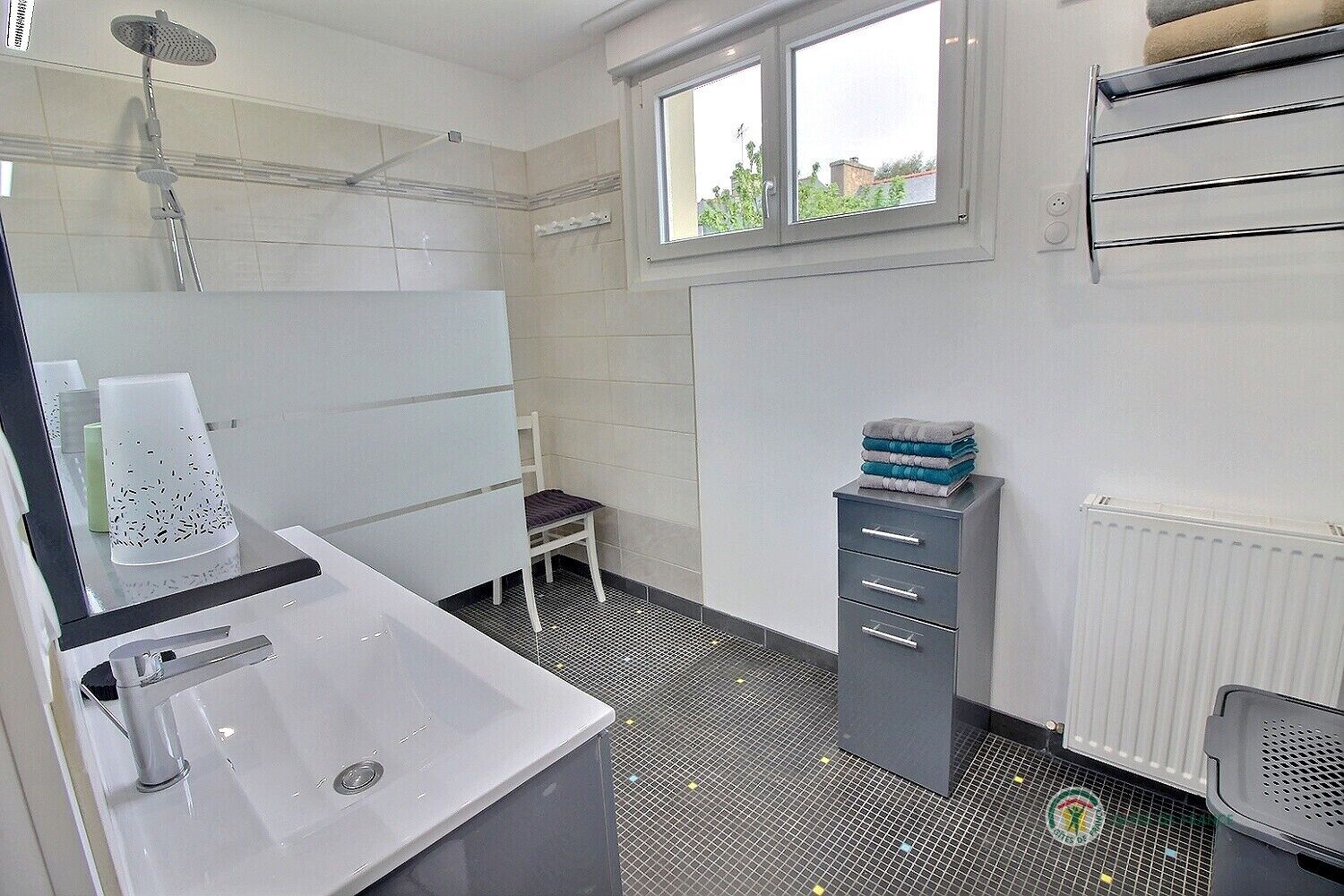 A modern bathroom with a white sink, a shower, a toilet, and a small window.