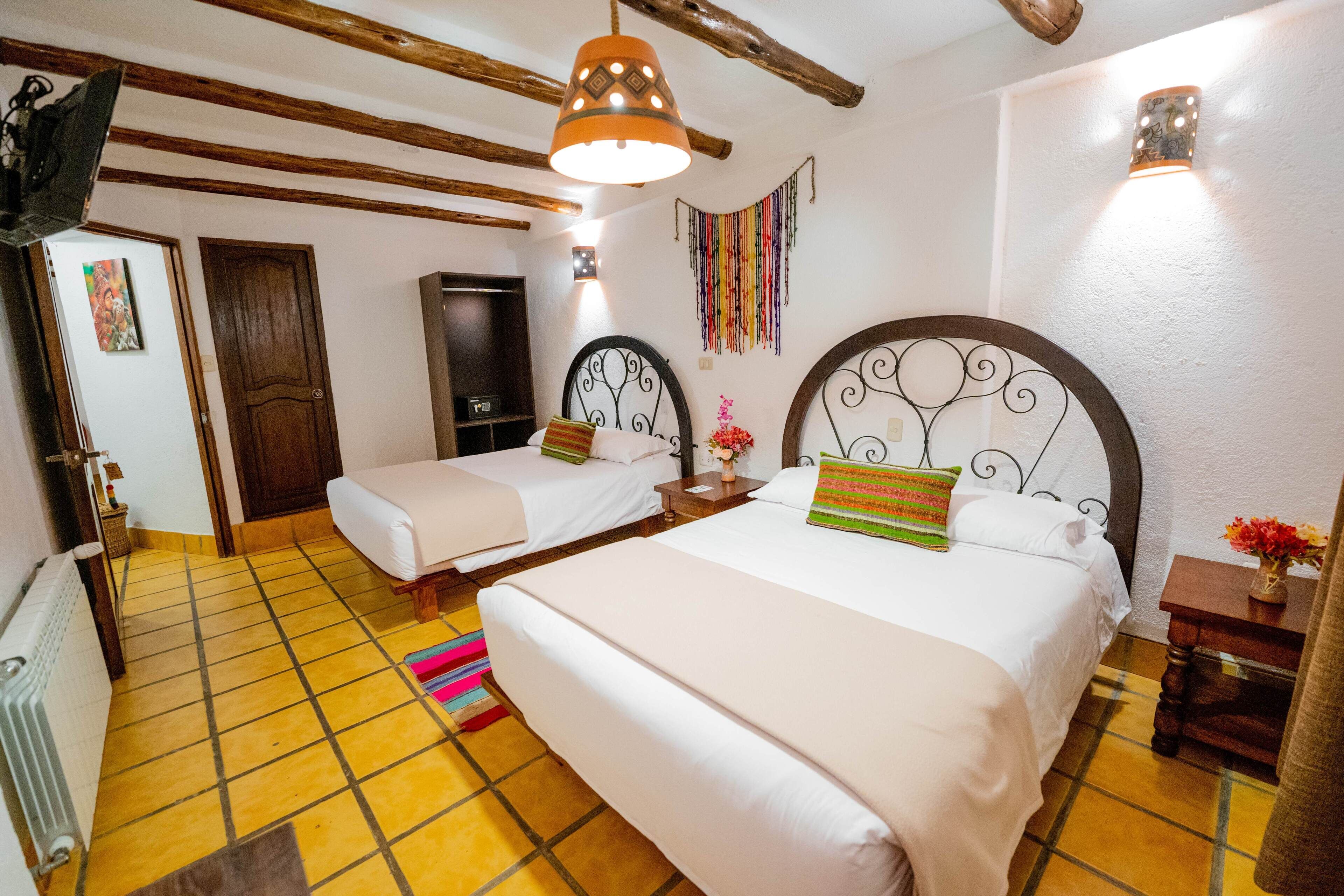 A hotel room with two beds, a wooden ceiling, a tiled floor, and a small table with a vase of flowers.