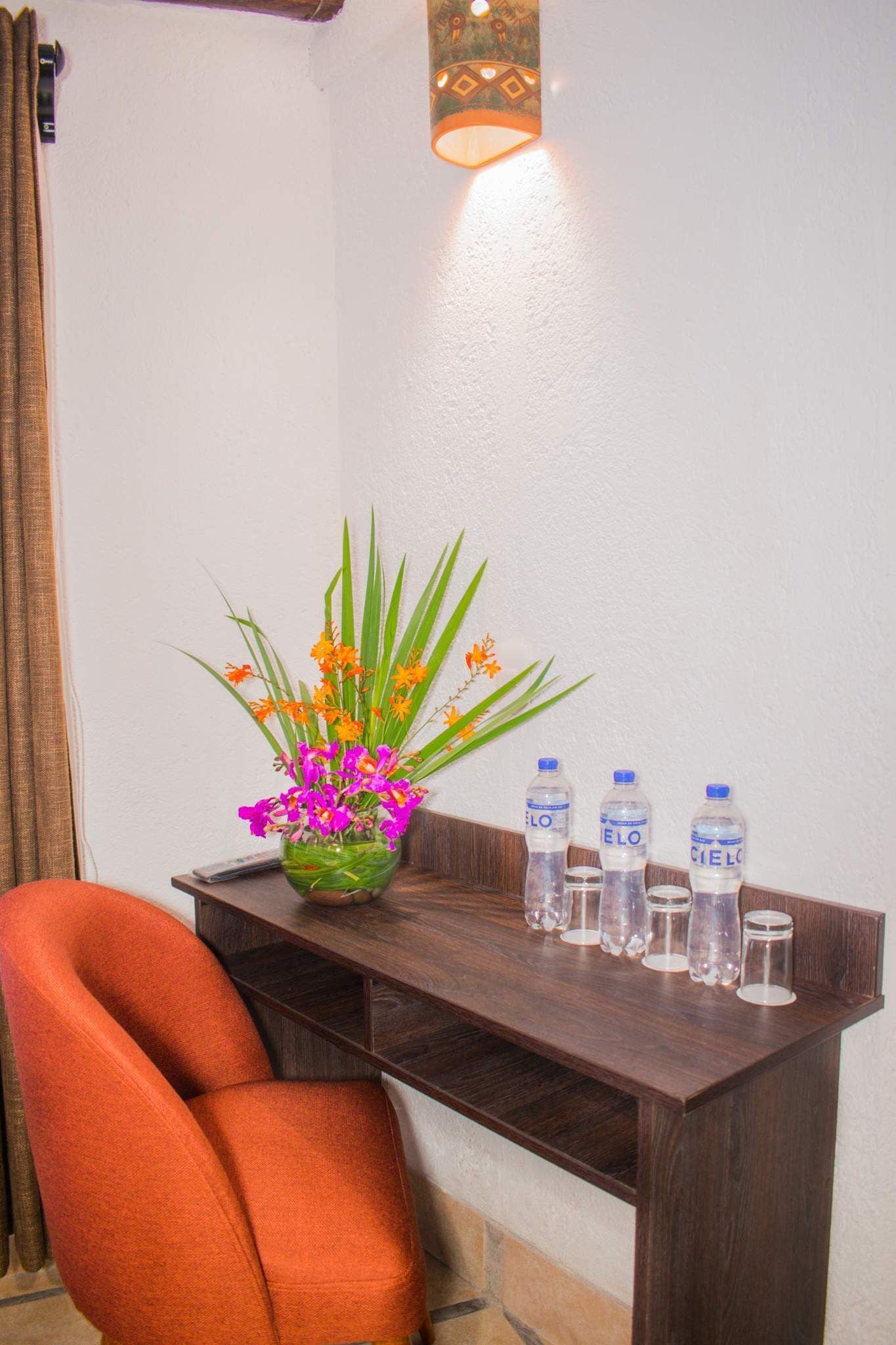 A corner desk with a vase of flowers, water bottles, and a remote control.