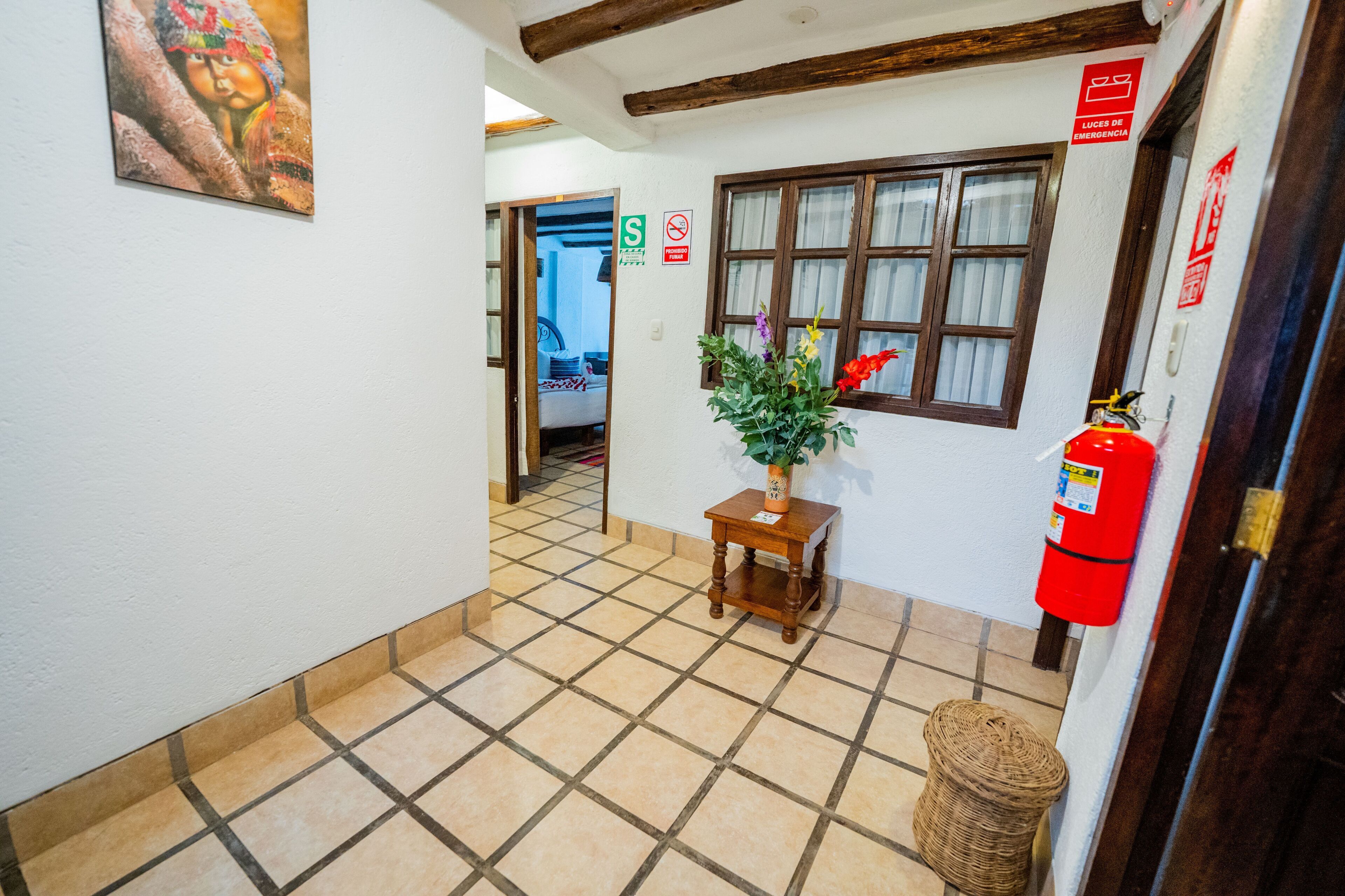 Un pasillo con piso de baldosas, una mesa de madera con una planta en maceta, un extintor y una puerta con un letrero rojo.