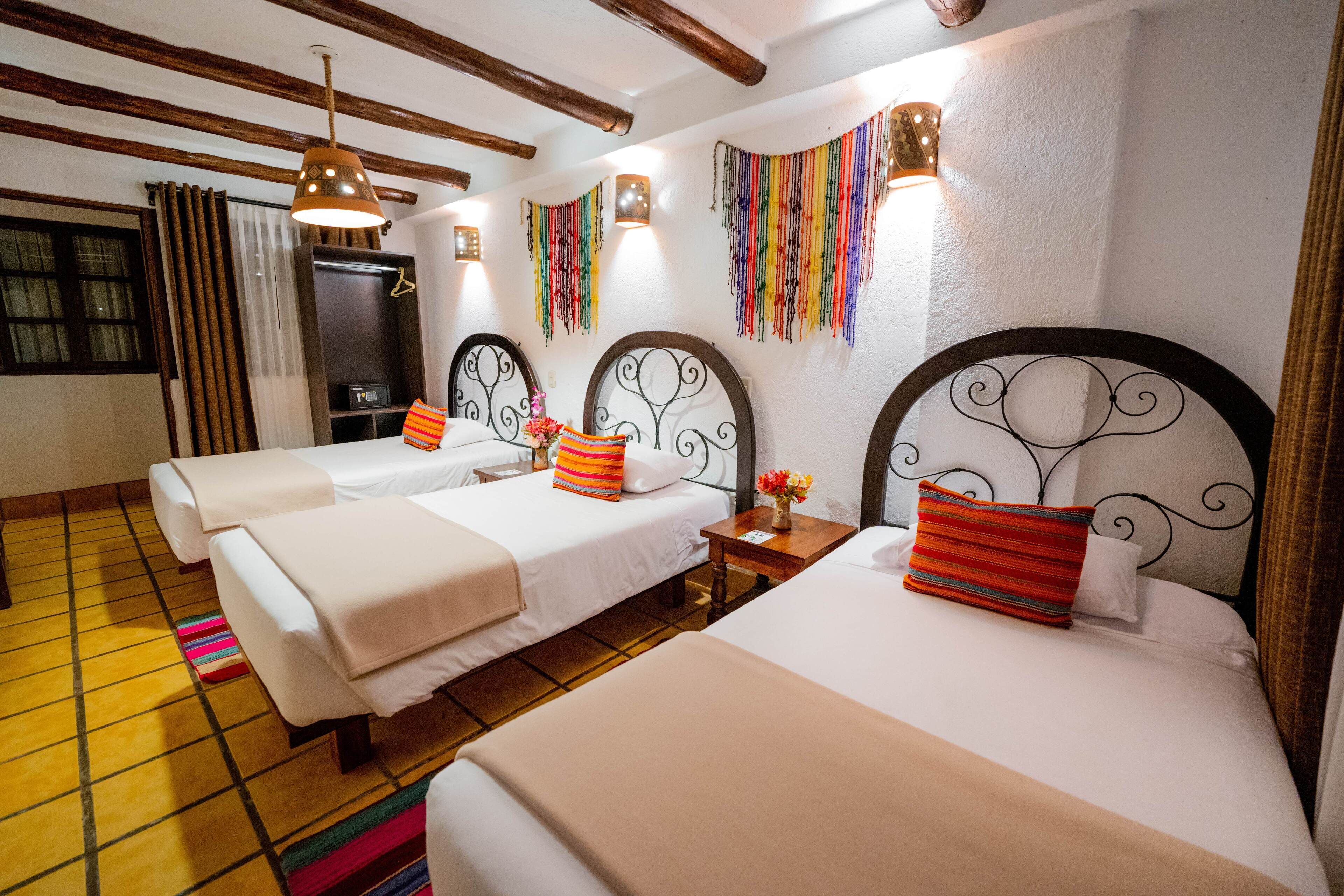 Una habitación de hotel con tres camas, vigas de madera en el techo y decoraciones de pared coloridas.