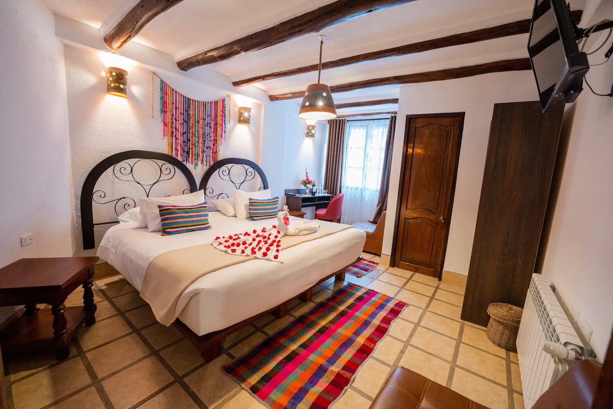 A bedroom with a bed, a bedside table, a hanging light fixture, and a window with curtains.