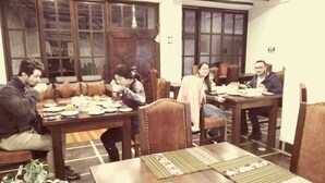 A dining area with wooden tables and chairs, large windows, and a plant on the floor. - Vilas Insight Hotel Machupicchu (Machu Picchu)