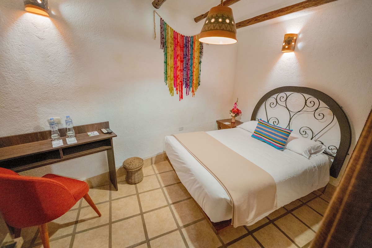 A bedroom with a bed, a desk, a chair, a lamp, and a wall decoration.