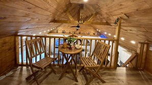 Ein Holzinnenraum mit Balkon, Holzstühlen, einem runden Tisch und einer Hängelampe.