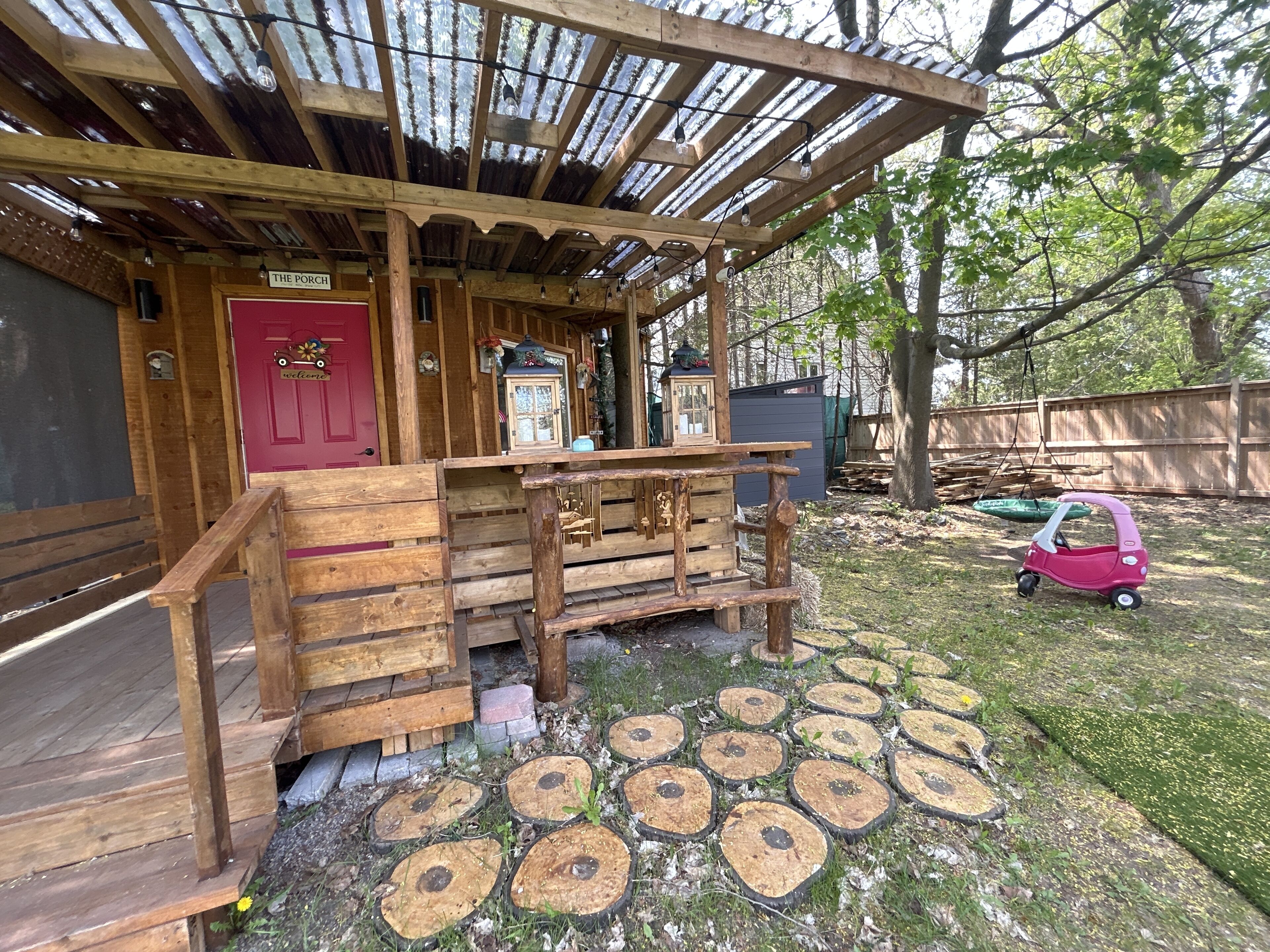 A rustic wooden structure with a red door, a porch, and a small car.