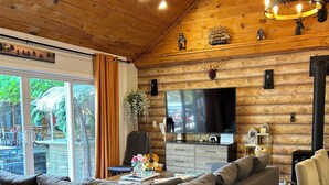 Ein gemütliches Blockhaus-Interieur mit einer Eckcouch, einem Flachbildfernseher und einem großen Fenster mit Blick auf einen tropischen Garten.