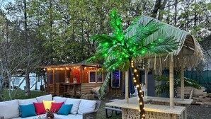 Eine Holzterrasse mit einem Korbsessel, einem Glastisch und einer kleinen Palme mit Lichterkette.
