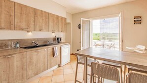 Eine moderne Küche mit Holzschränken, einer Spüle und einem Geschirrspüler. Es gibt einen Essbereich mit Tisch und Stühlen sowie einen Blick auf einen Garten durch eine Schiebetür.