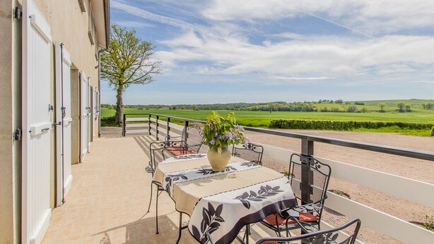 Eine Terrasse mit Esstisch, mit Blick auf eine grüne Landschaft.