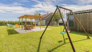 Ein Garten mit einer Holz-Schaukel, einem überdachten Esstisch und Gartenstühlen.