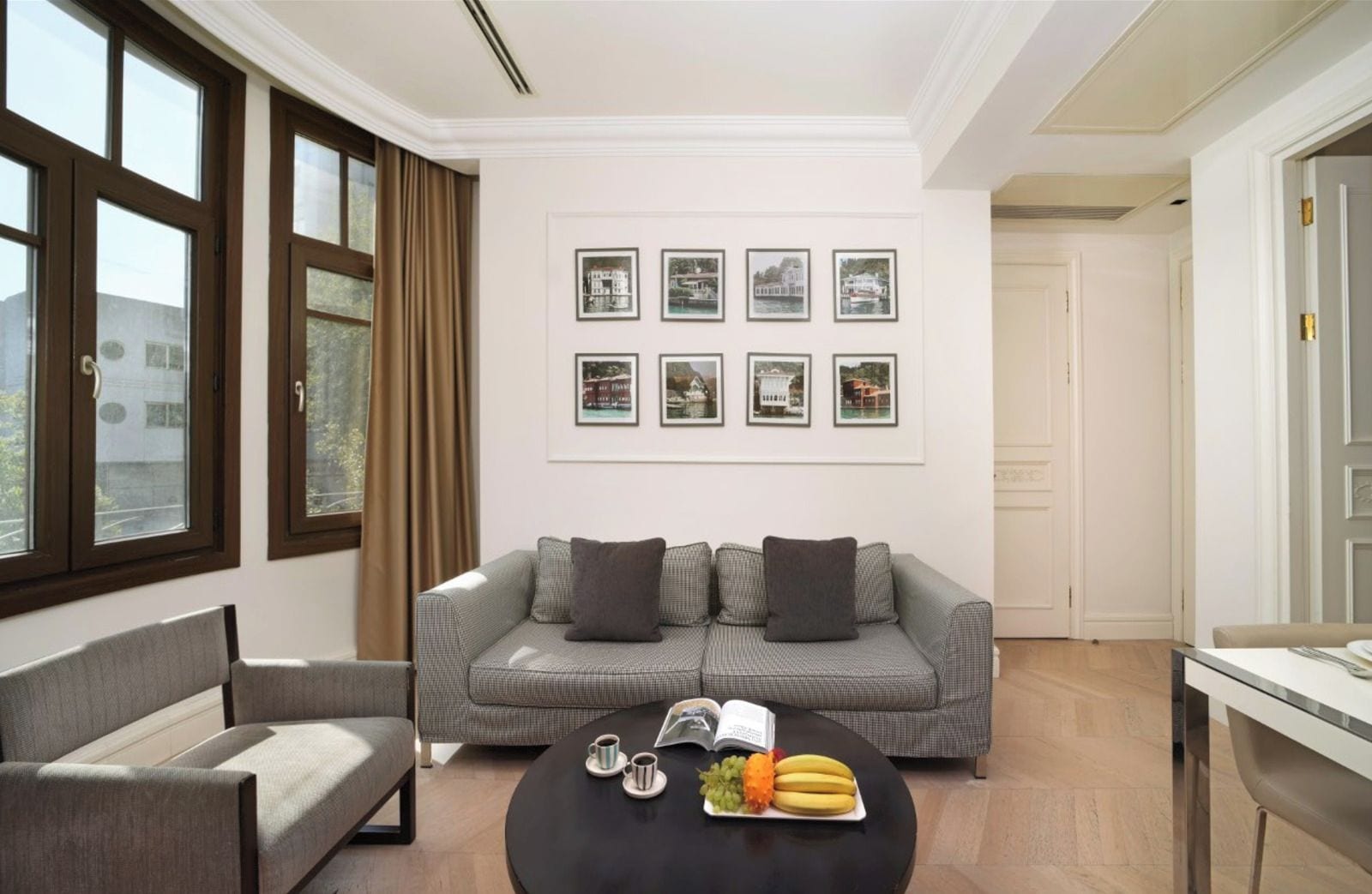 Un salon moderne avec un canapé gris, une table basse ronde sur laquelle on peut voir des fruits et un livre, et des tableaux encadrés accrochés au mur.