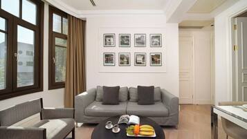 Un salon moderne avec un canapé gris, une table basse ronde sur laquelle on peut voir des fruits et un livre, et des tableaux encadrés accrochés au mur.