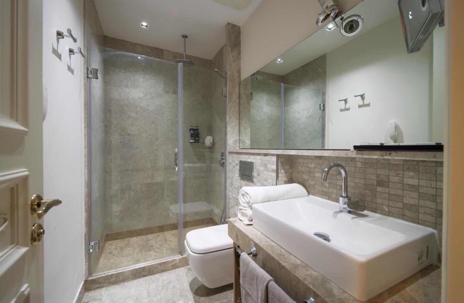 A modern bathroom with a glass-enclosed shower, a white sink, and a large mirror.