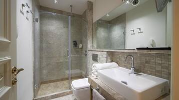 Un baño moderno con ducha envuelta en vidrio, lavamanos blanco y un espejo grande.