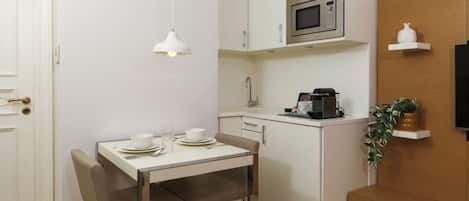 A compact kitchen with a dining table, chairs, a microwave, a coffee machine, and a small potted plant.