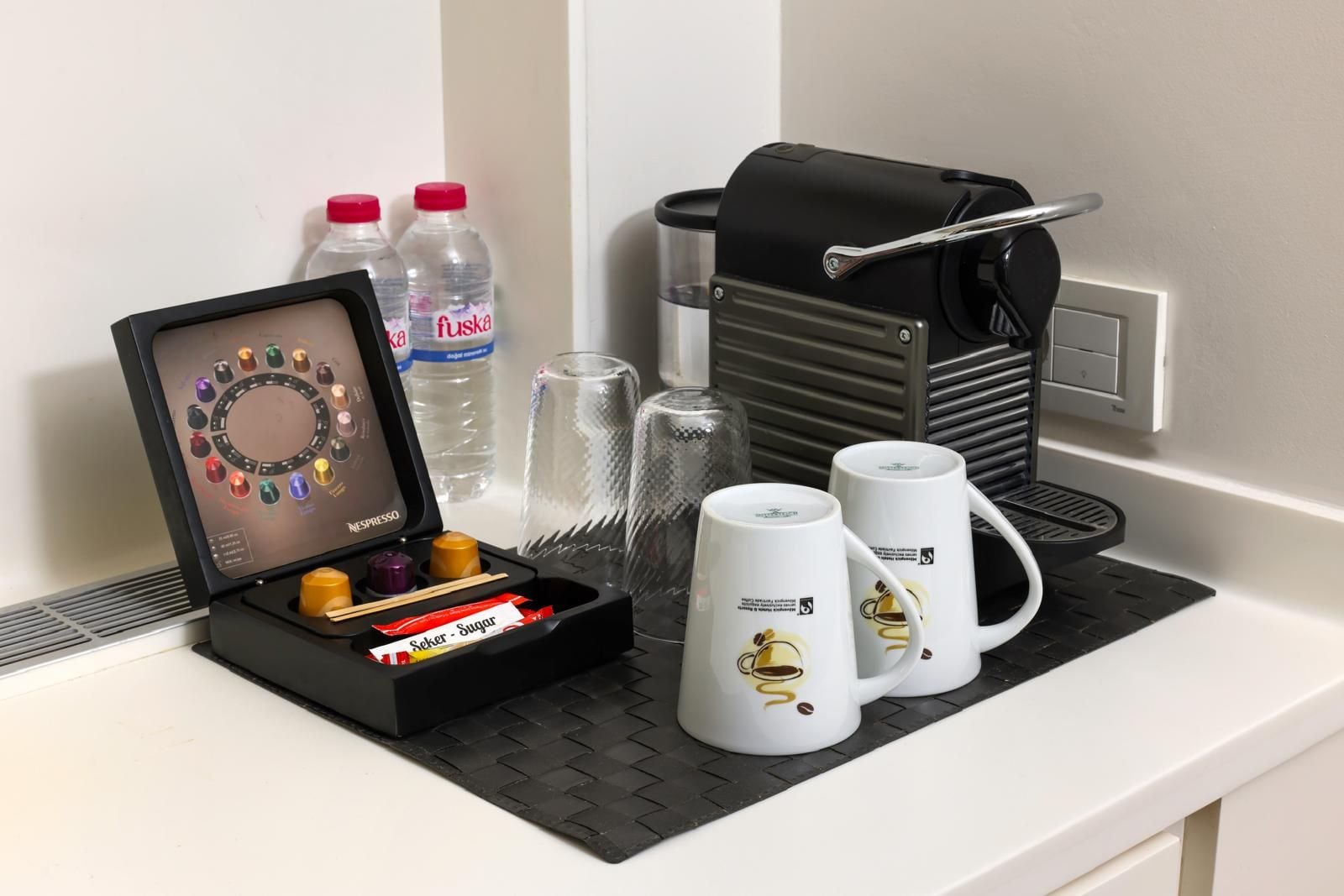 A coffee machine with a drip tray, two water bottles, a coffee grinder, and two coffee mugs on a countertop.