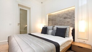 A modern bedroom with a large bed, a headboard with a textured wall, bedside lamps, and a wooden nightstand. - Atik Suite Taksim  (Istanbul)