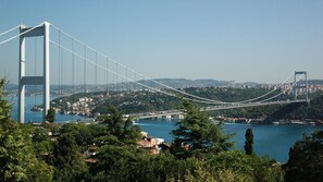 A suspension bridge spanning a body of water with surrounding greenery and a distant cityscape. - Atik Suite Taksim  (Istanbul)