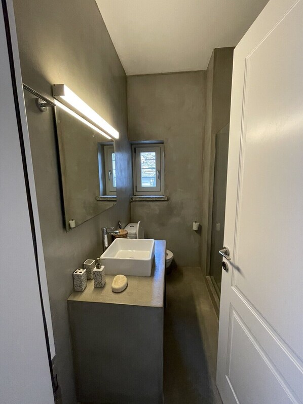 A compact bathroom with a white sink, a mirror, and a window.