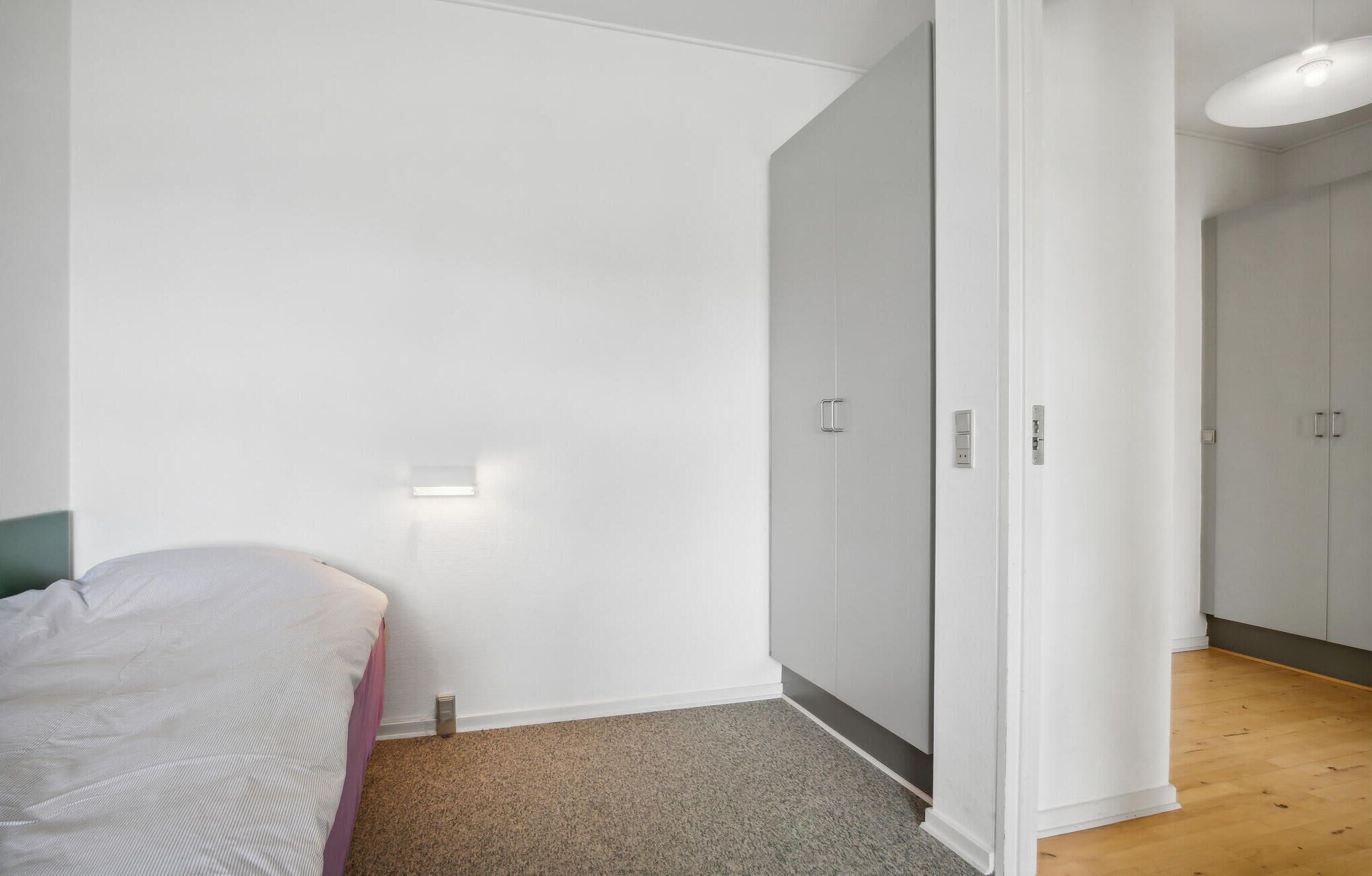 Quarto com uma cama, guarda-roupa e luminária na parede.