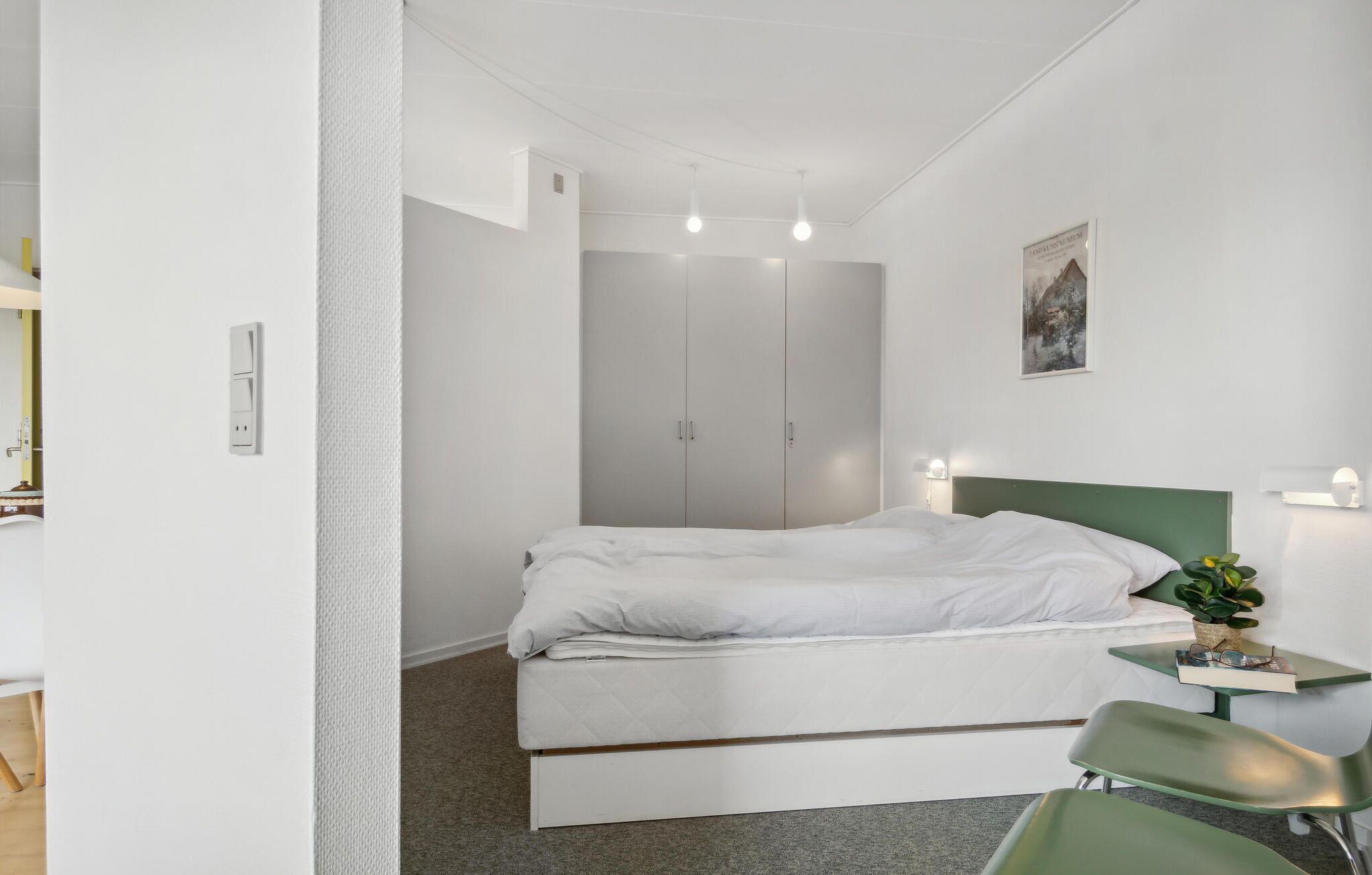Een slaapkamer met een bed, een groen hoofdeinde, een nachtkastje met een lamp en een groene stoel.