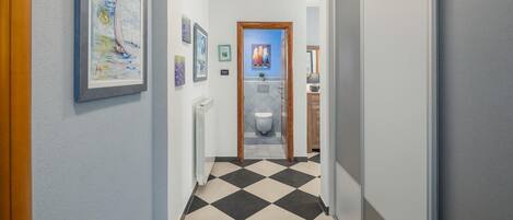 Een gang met een zwart-wit betegelde vloer die leidt naar een badkamer met toilet en wastafel.
