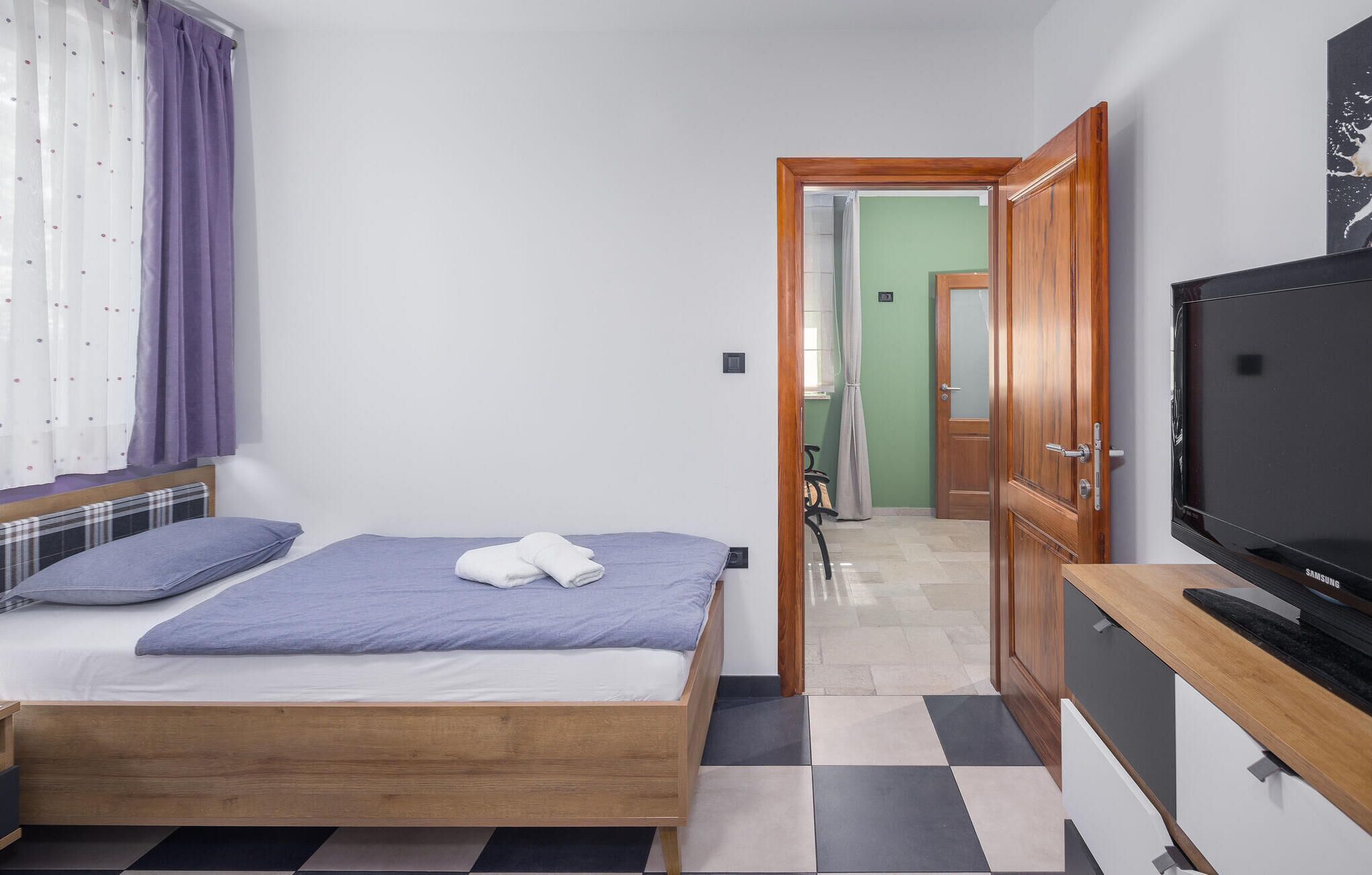 A bedroom with a bed, a television, and a bathroom visible through an open door.