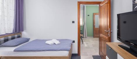 A bedroom with a bed, a television, and a bathroom visible through an open door.
