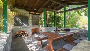 An outdoor patio with a stone fireplace, wooden table, and benches. - Nice apartment in Buzet (Buzet)