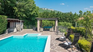 A swimming pool with lounge chairs and a pergola, surrounded by greenery and a mountain view. - Nice apartment in Buzet (Buzet)