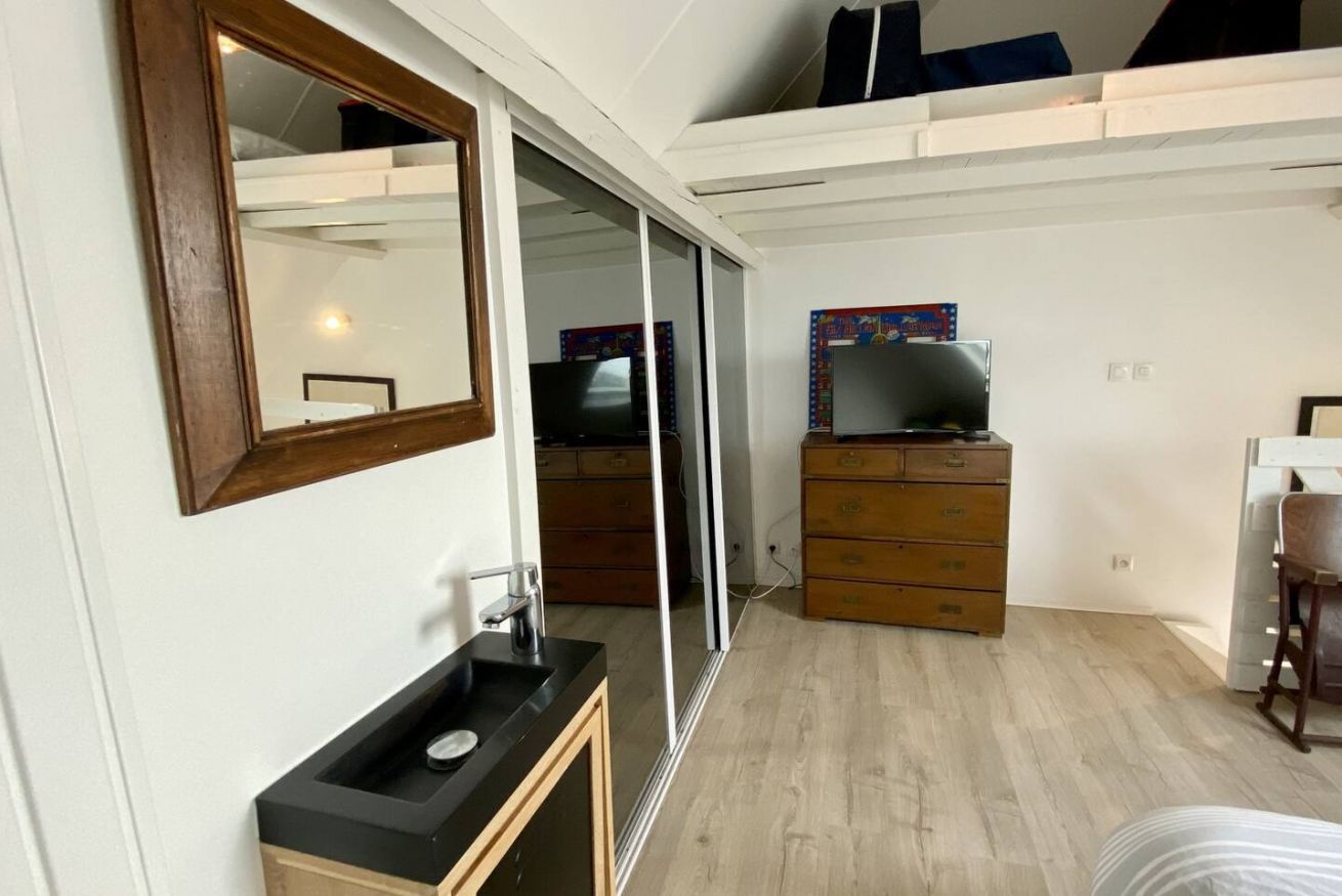 A bedroom with a large mirror, a black sink, a wooden dresser, a television, and a bed.