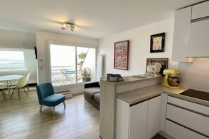 A modern kitchen with a dining area, a blue chair, and a large window. - Appartement Avec Terrasse , Surplombant la Baie de Somme (Le Crotoy)